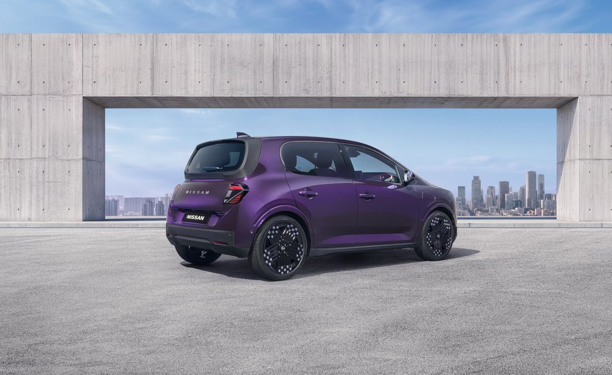 Three-quarter rear view of a purple Nissan PIXO electric city car parked beneath a modern concrete structure, with a city skyline in the background.