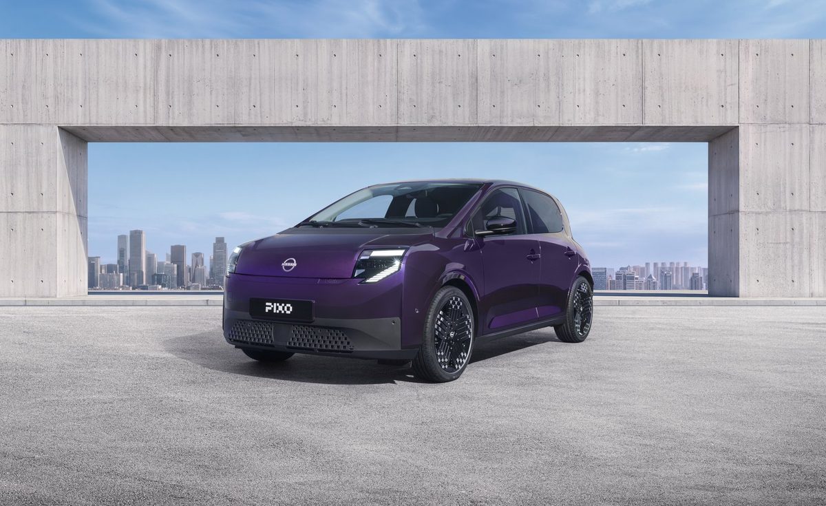 Three-quarter front view of a purple Nissan PIXO electric city car parked beneath a modern concrete structure, with a city skyline in the background.